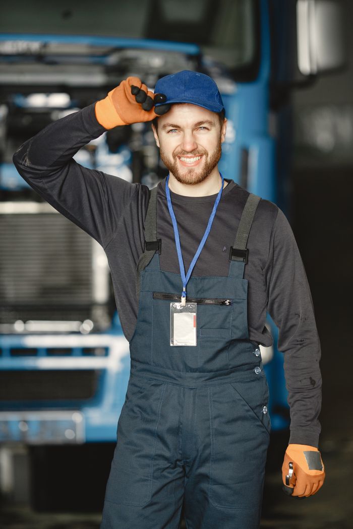 Friendly mechanic in uniform saluting in front of a truck at workplace.